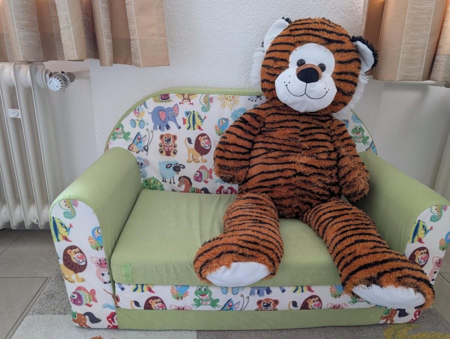 Grünes Kindersofa mit Tiermuster, darauf ein großer Stofftiger