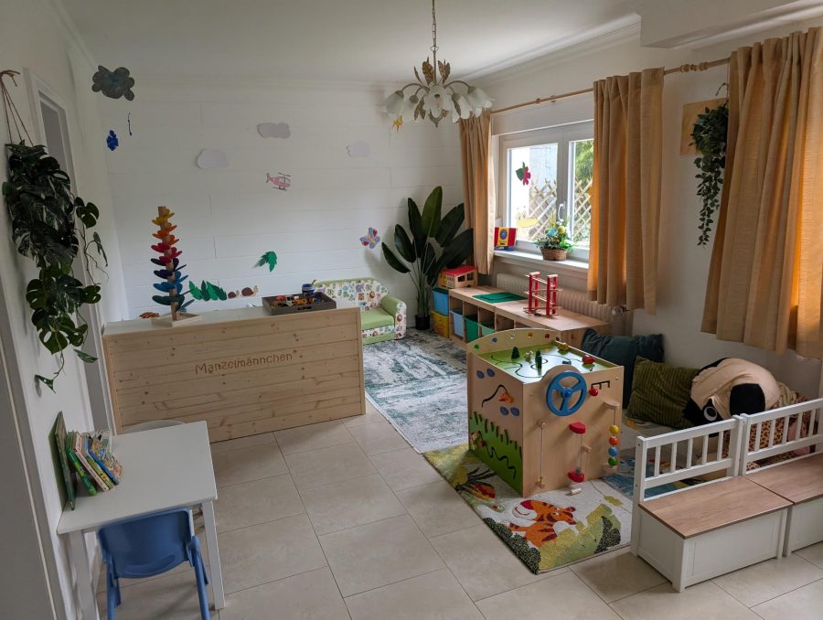 Gruppenraum mit hölzernem Raumteiler, buntem Kugelbaum, grünem Sofa und einem Spielwürfel mit Lenkrad