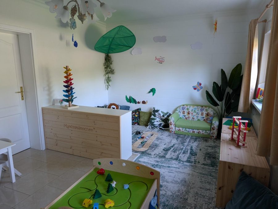 Kissenecke mit Sofa, Holzeisenbahn auf dem Teppich und Spieltisch im Vordergrund